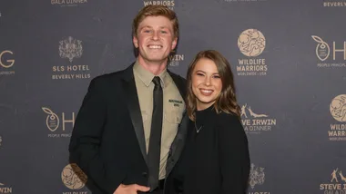 Young man and woman smiling in front of a Wildlife Warriors event backdrop.