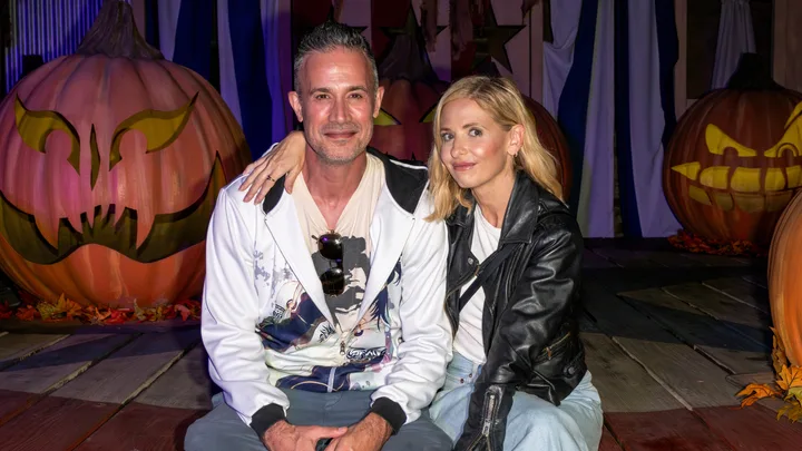 A couple sitting together, surrounded by decorative pumpkins with carved faces, in a festive Halloween setting.