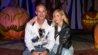 A couple sitting together, surrounded by decorative pumpkins with carved faces, in a festive Halloween setting.