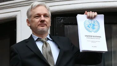 Man holding a United Nations Human Rights Council document, wearing a suit and standing outdoors.