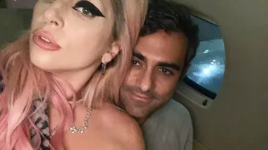 A woman with pink hair and bold eyeliner poses with a man in a dimly lit setting, likely inside a vehicle.