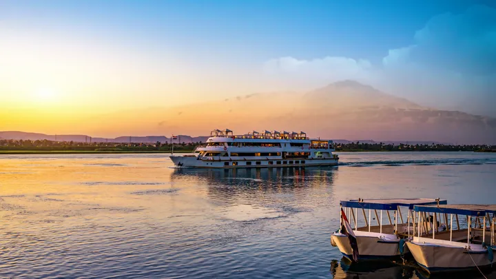 Cruise ship on the Nile River at sunset, with two smaller boats in the foreground.