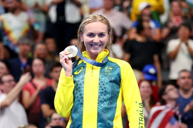 Australia's female athlete in yellow-green attire smiling, holding a silver medal at Olympic event with crowd cheering.