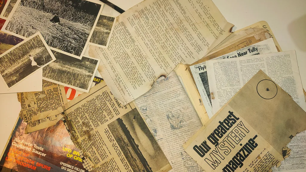 Old newspapers and photos about the crop circle in Tully, Australia, spread on a table.