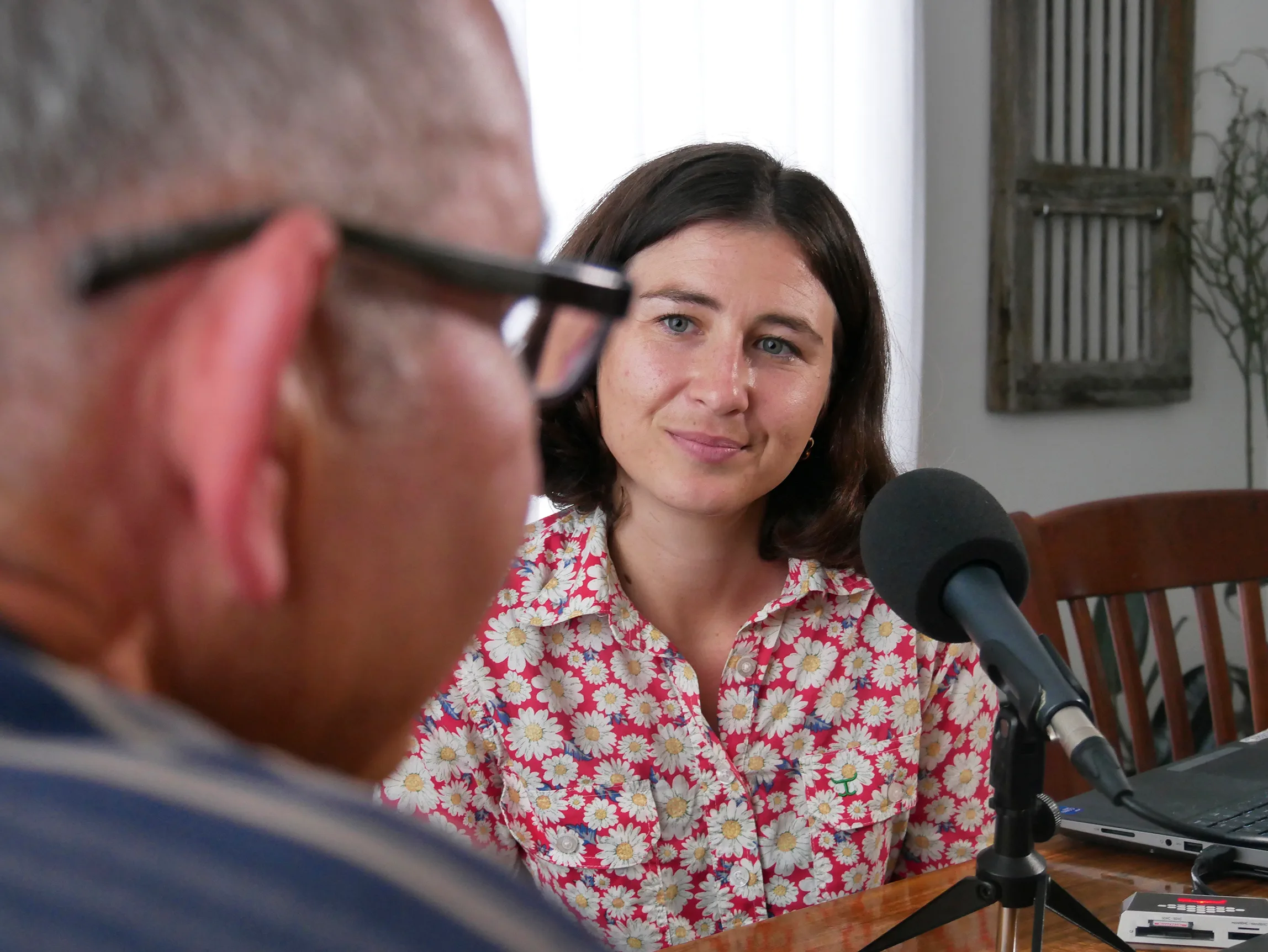 A woman sits at a table with a microphone, interviewing a man.