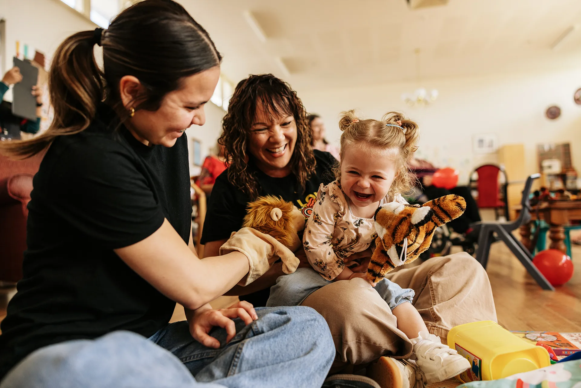 Two woman and a young girl sitting on the floor surrounded by toys.