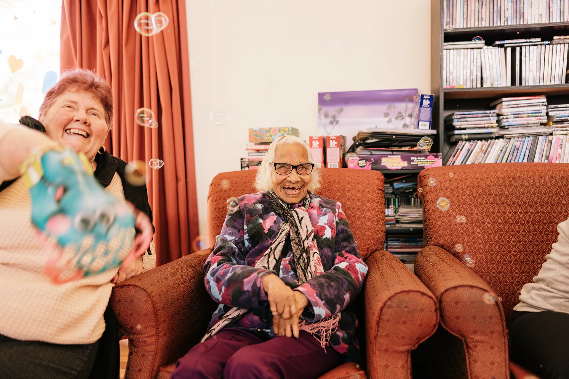 Two older woman smiling as bubbles are blown around them.