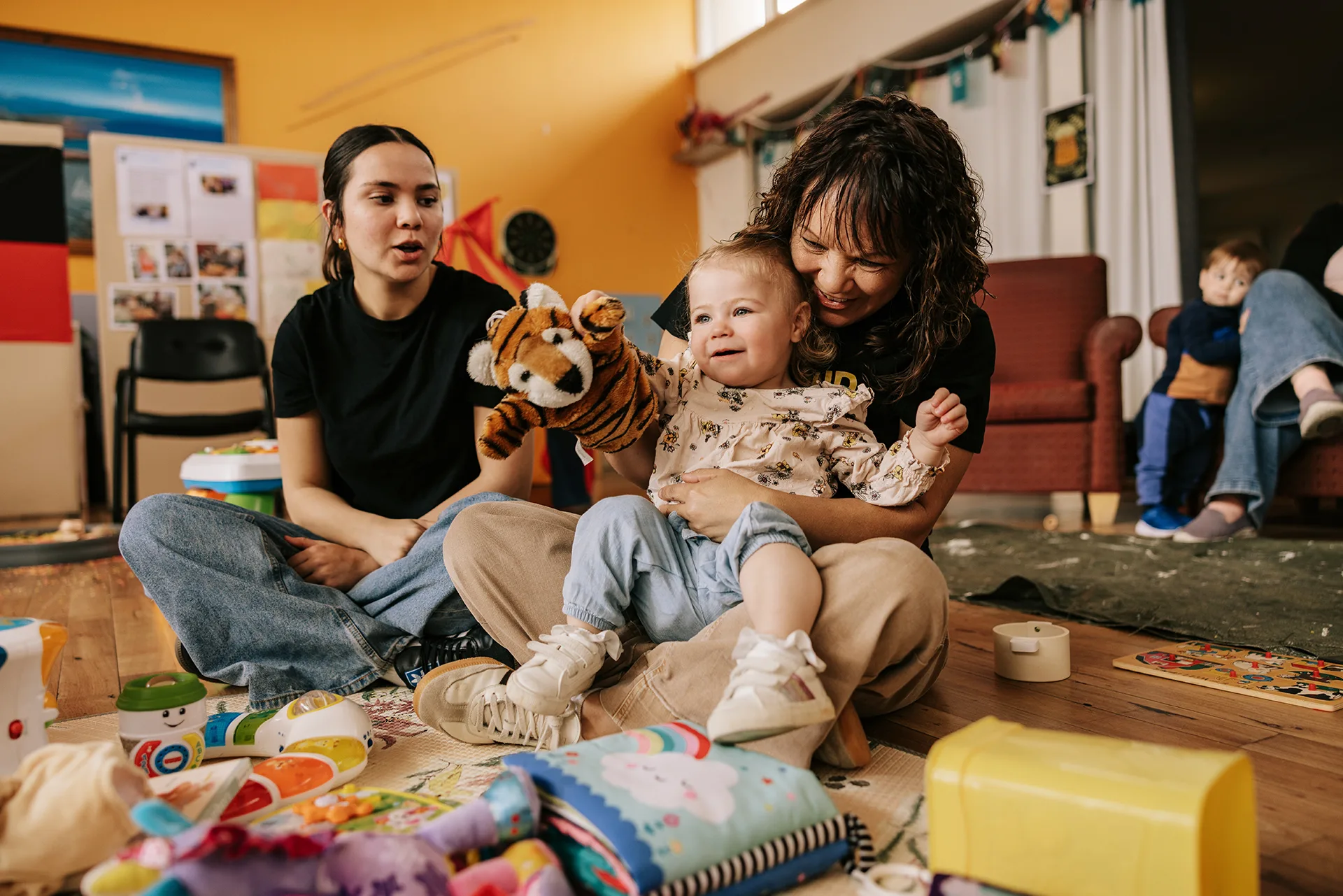 Two woman and a young girl sitting on the floor surrounded by toys.