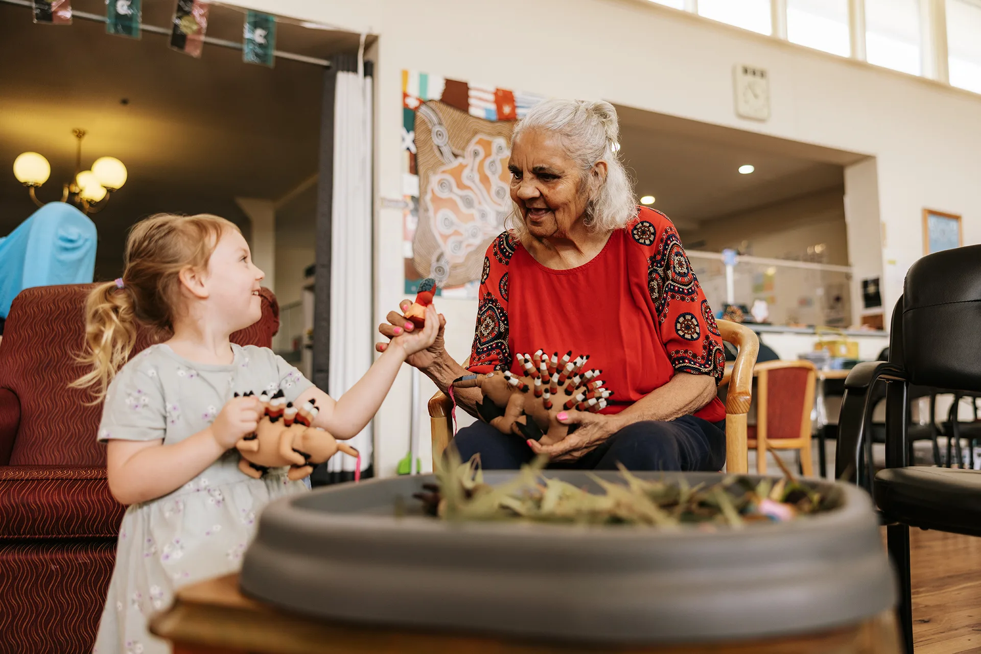 A young woman passes a toy to an older woman.