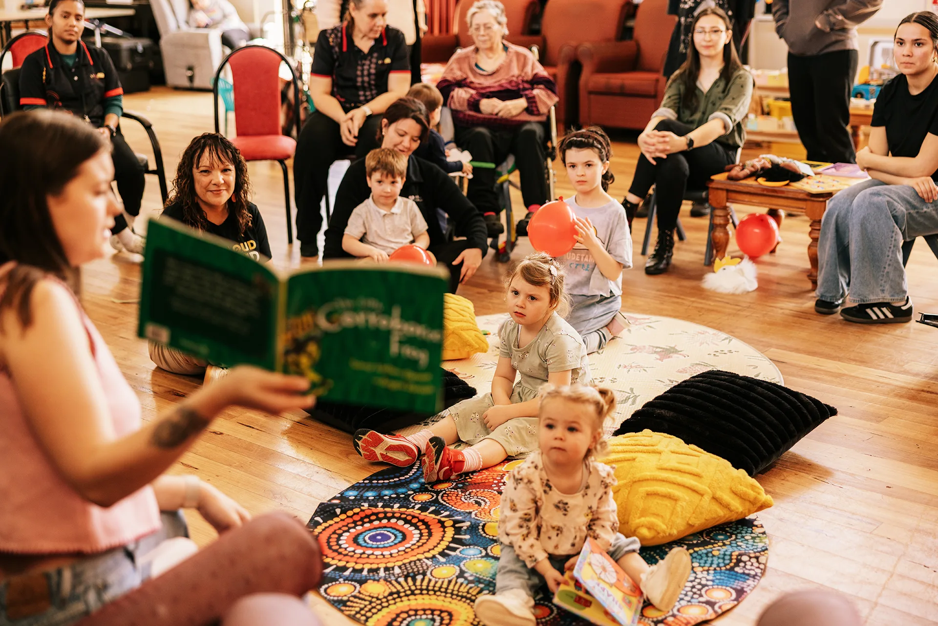 A woman reads a book to a group of children and adults at an intergenerational playgroup.