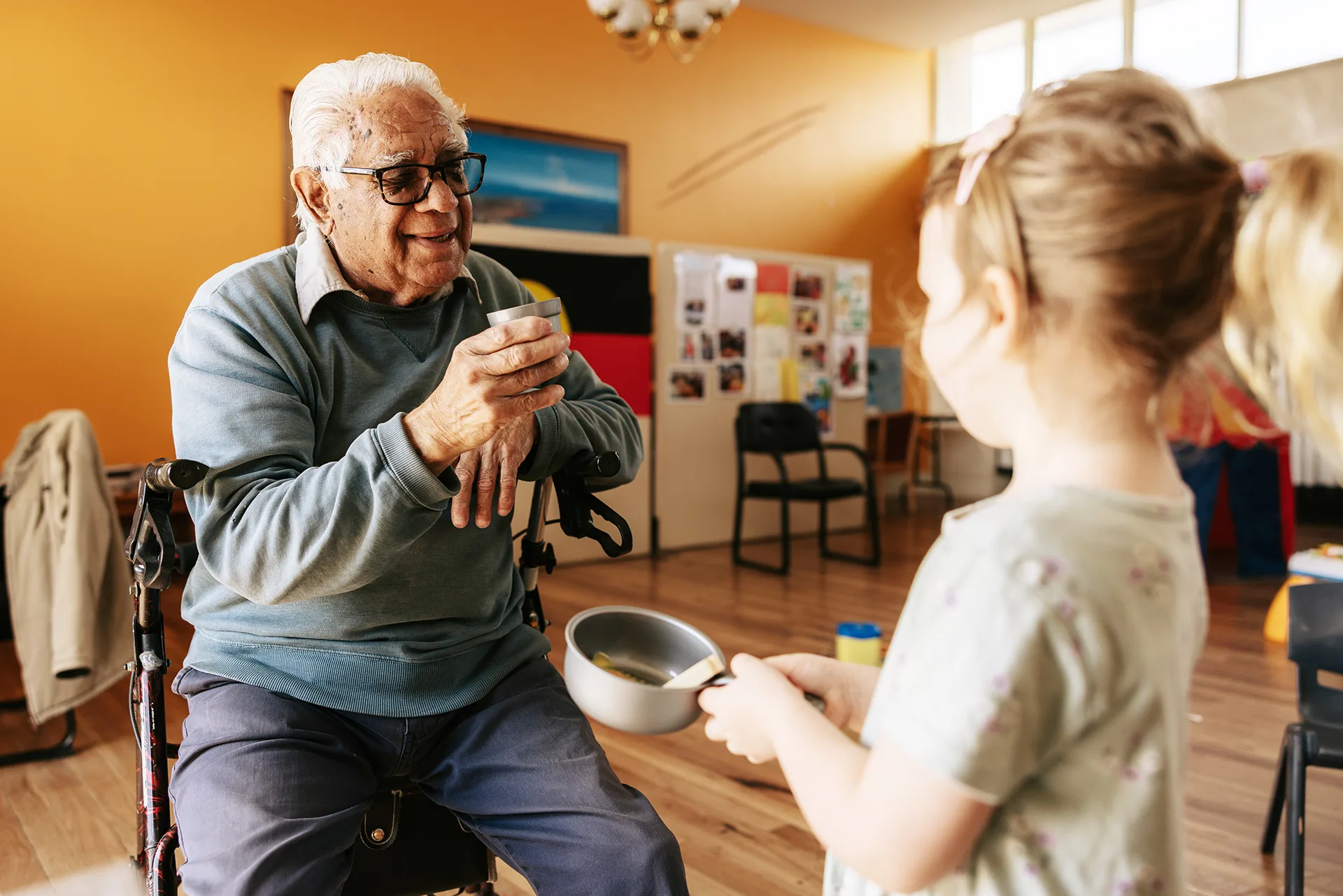 An older man on a walker smiling at a young girl during an intergenerational playgroup.