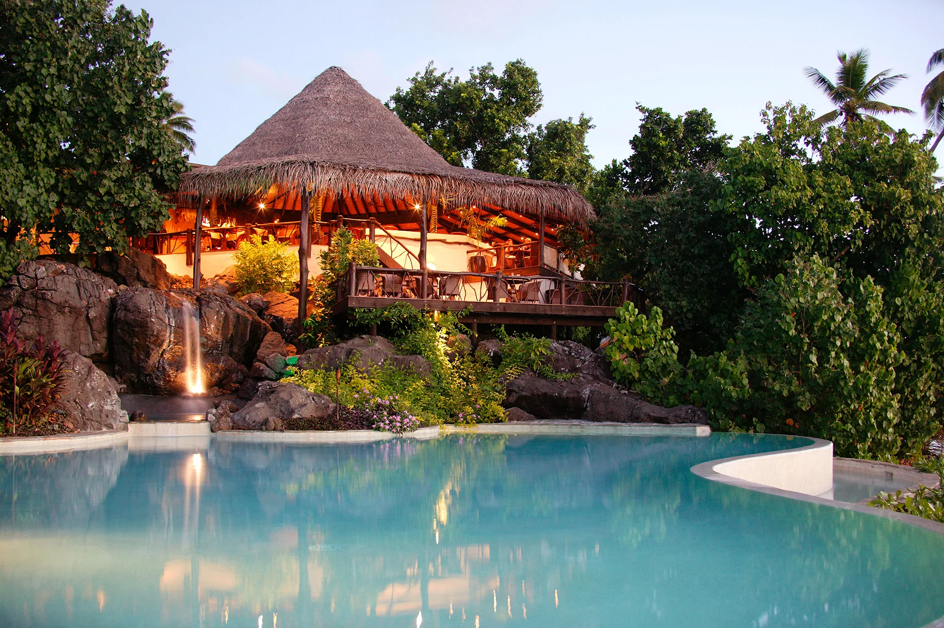 A thatched-roof bungalow in front of a swimming pool