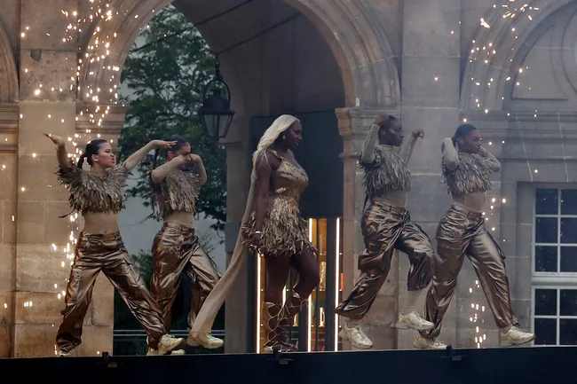 Performers in gold outfits dance with sparklers in an archway setting.