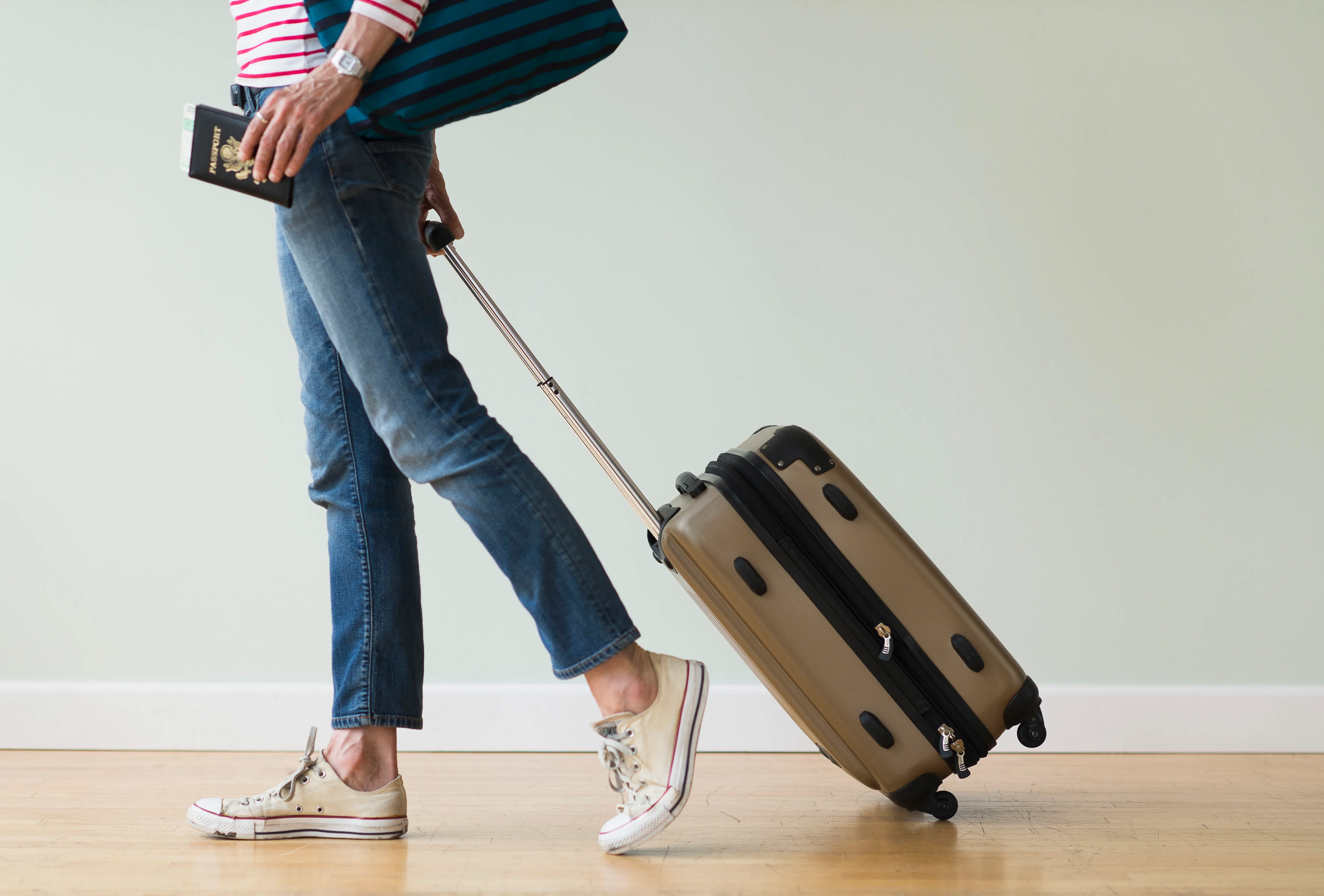 Lady in jeans and sneakers wheeling a suitcase and carrying a passport