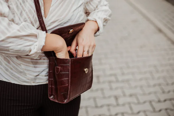 Woman reaching into a brown leather handbag on a cobblestone street, wearing a striped blouse and ring.