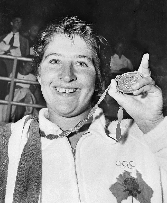 Smiling athlete holding an Olympic medal, wearing a jacket with Olympic rings and an Australian symbol.