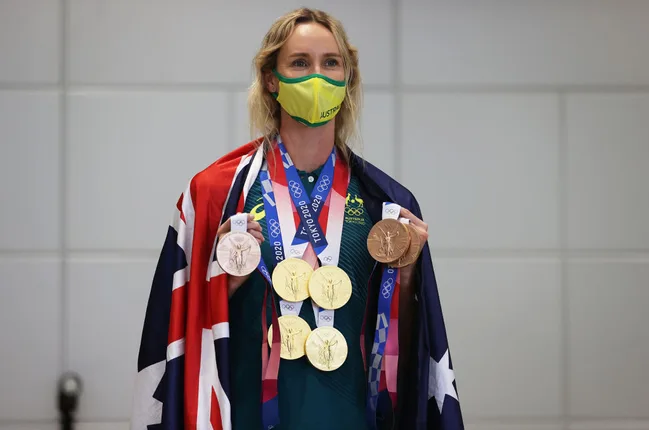 Australian athlete in a mask and flag holds several Olympic medals, including gold, silver, and bronze, from Tokyo 2020.