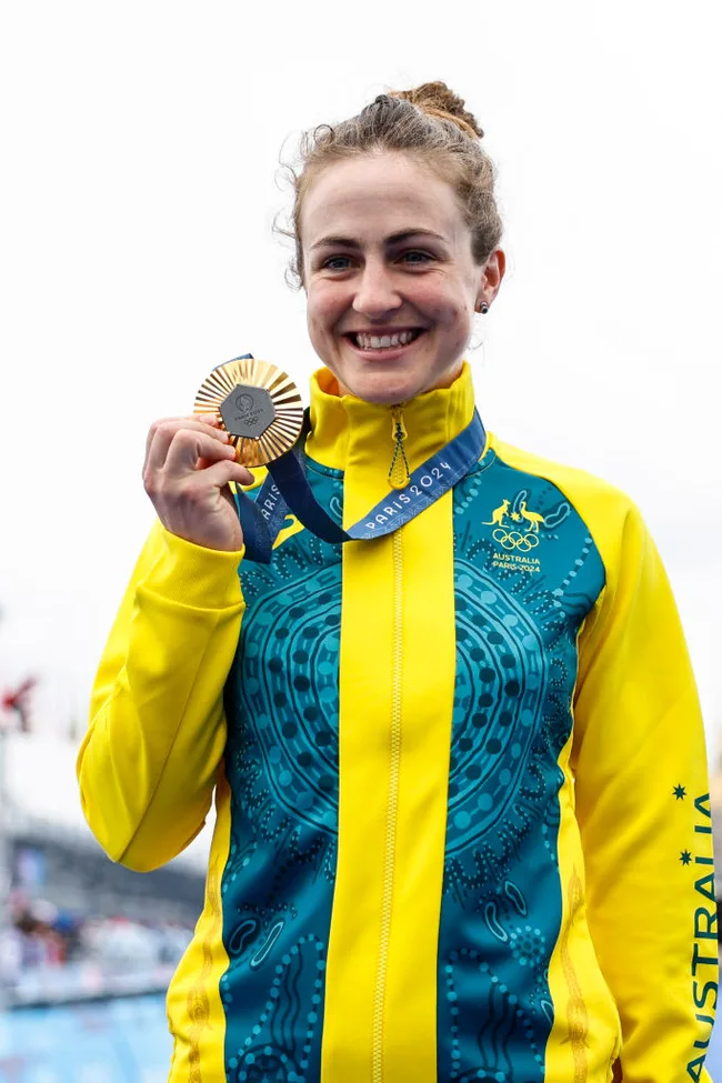 Smiling athlete in Australian jacket holds Olympic gold medal, Paris 2024.