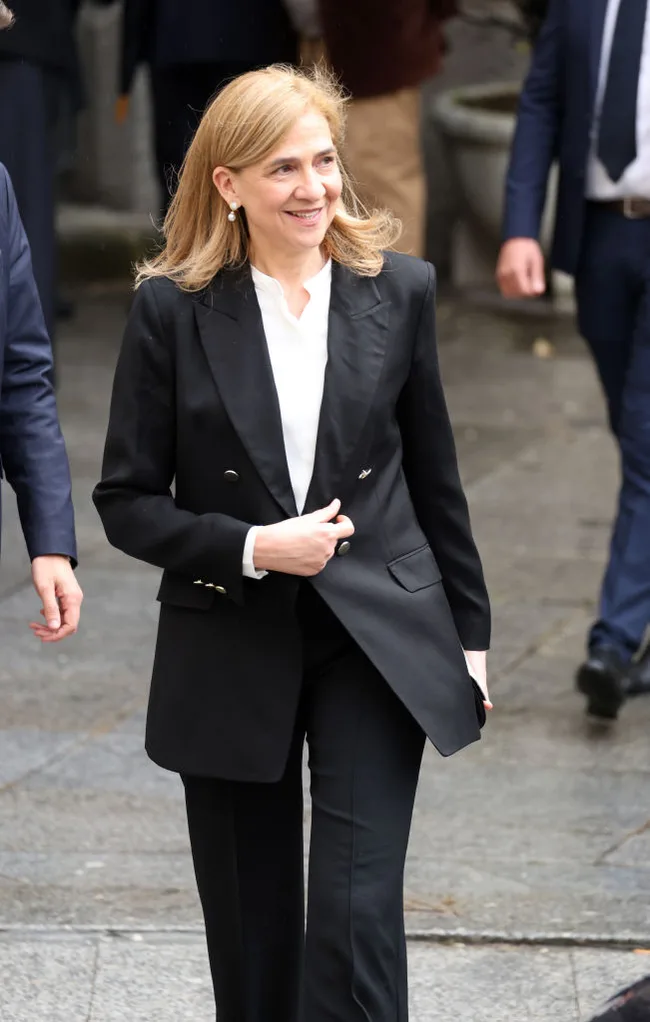 A woman in a black suit walks outdoors, smiling, accompanied by others in business attire.