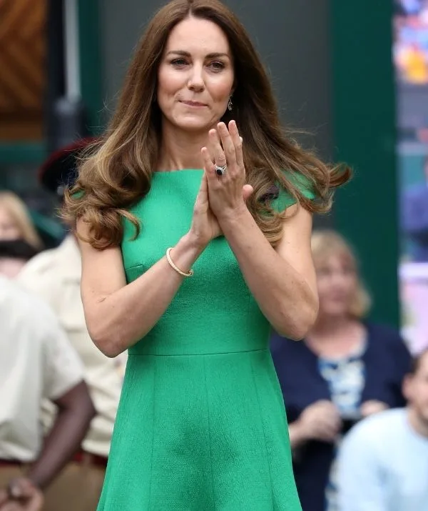 Woman in green dress clapping, with long brown hair, outdoors.