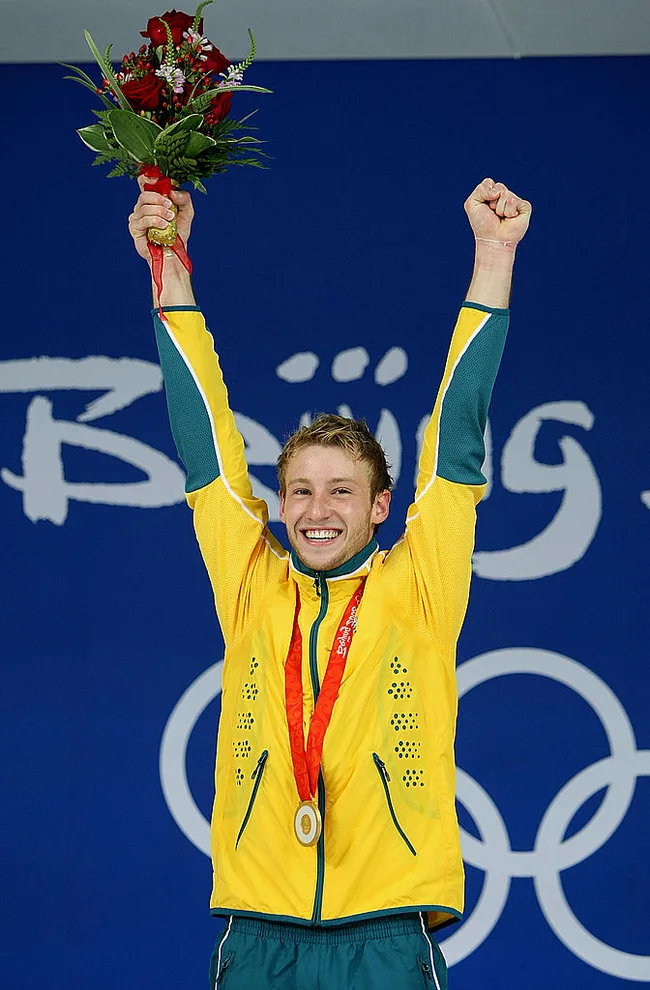 Australian athlete celebrates with a gold medal and bouquet, wearing a yellow jacket, at the Beijing Olympics.