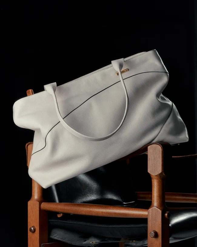 White leather tote bag on a wooden chair, against a dark background.