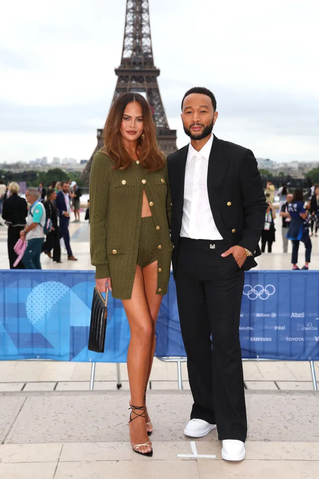 A couple posing in front of the Eiffel Tower, with the woman in a green outfit and the man in a black suit.