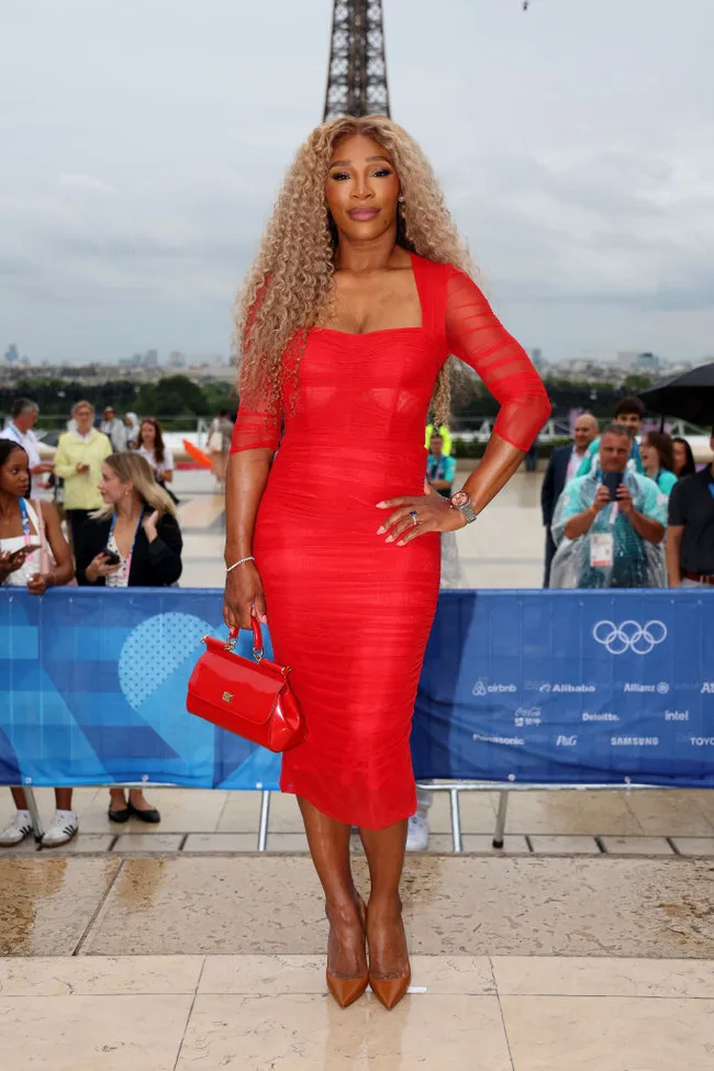 A woman in a red dress poses confidently in front of the Eiffel Tower, holding a matching handbag.
