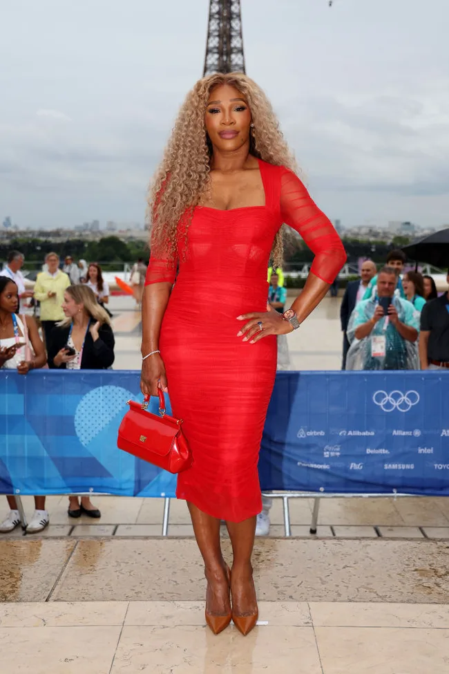 A woman in a red dress poses confidently in front of the Eiffel Tower, holding a matching handbag.