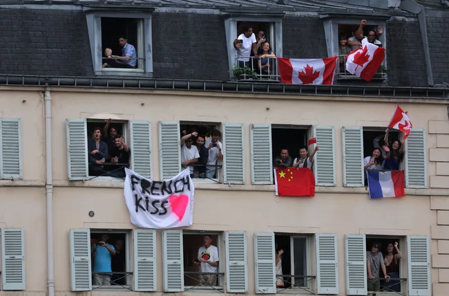 People in windows display various flags, including Canadian and Chinese. A banner reads "French Kiss" with a pink heart.