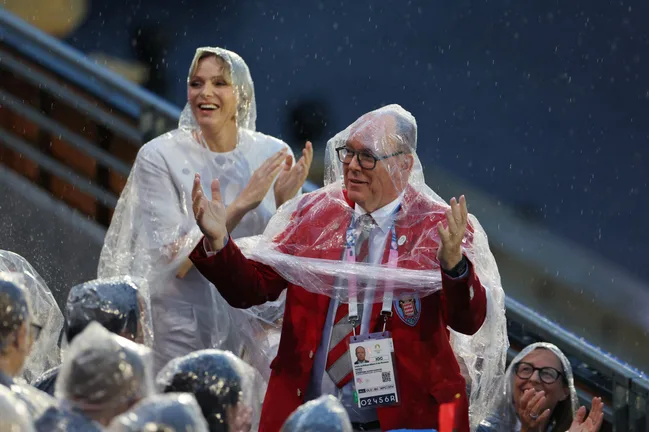 Two people in plastic ponchos smiling and clapping in the rain at an outdoor event.