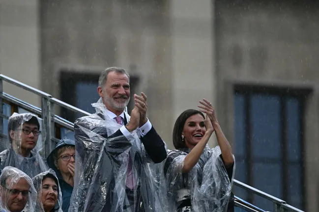 People in rain ponchos clapping in the rain at an outdoor event.