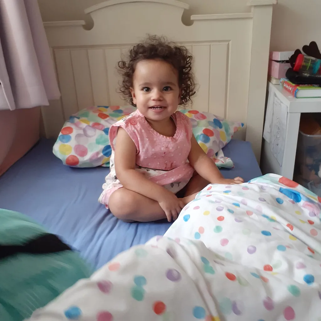 Tahlia sitting on her bed wearing a spotty pink dress.