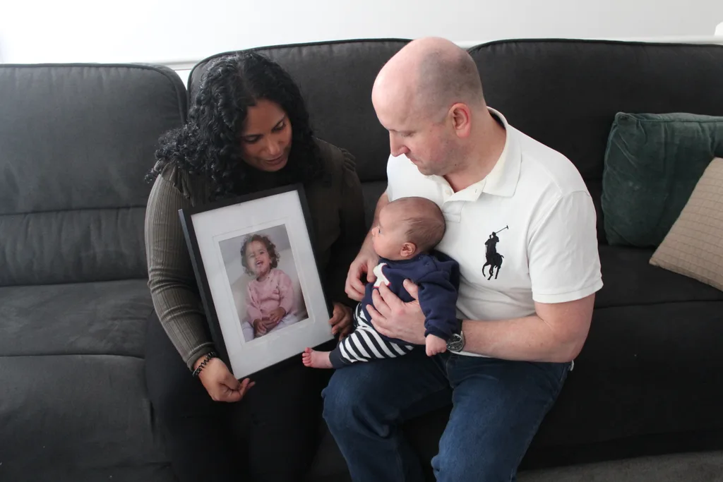 Yasmine holds a photograph of Tahlia, and Jason holds baby Tate on his lap.