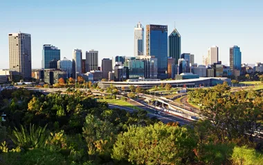 Skyline of Perth, Australia with modern skyscrapers and lush green foreground under a clear blue sky.