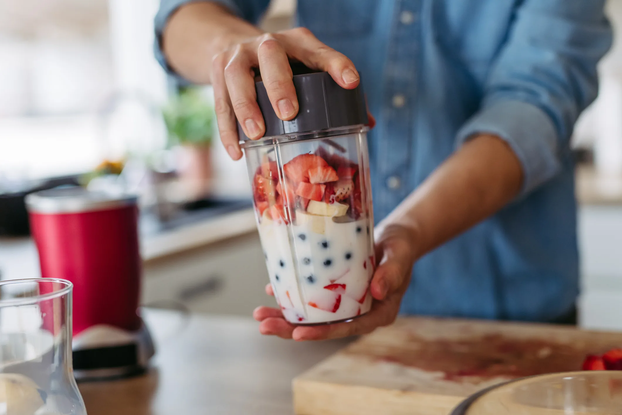 Close up of hands holding smoothie blender bottle with fruits and milk for healthy fruit smoothie.