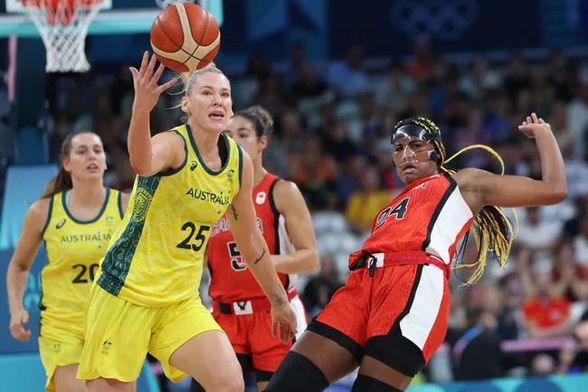 Australian basketball player in yellow challenges opponent in red during a game, reaching for the ball.
