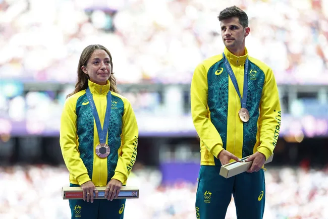Two Australian athletes standing with medals on their necks during a sports ceremony, wearing team jackets.