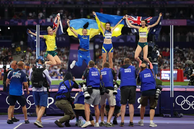 Athletes celebrate on podium, holding Australian and Ukrainian flags, surrounded by photographers at Paris 2024 Olympics.