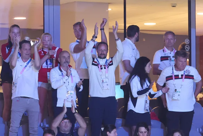 A group of people in sports attire clapping and cheering at an indoor event, displaying badges and lanyards.