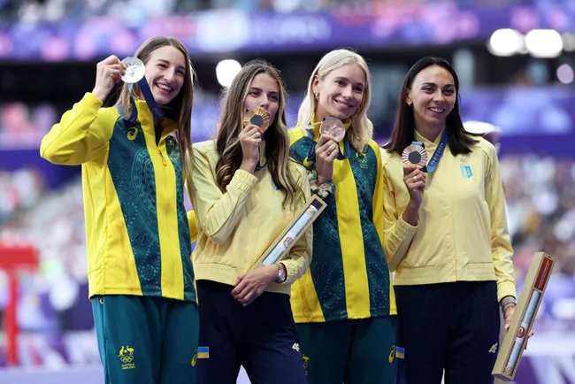 Four female athletes on a podium, each holding medals, wearing team uniforms with blue and yellow accents.