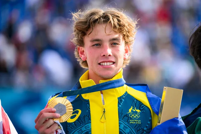 Australian athlete with a gold medal, wearing a yellow and blue jacket, smiling at an outdoor event.