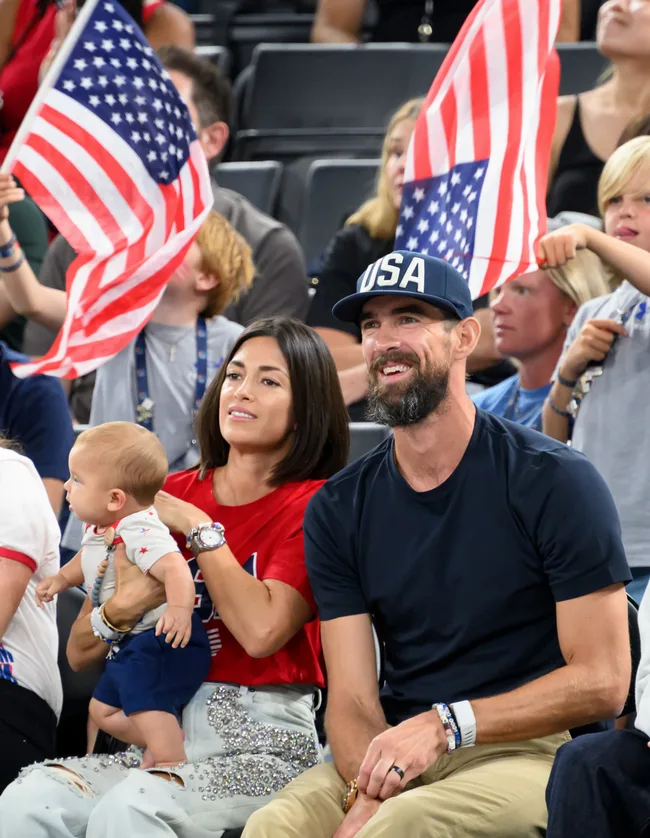A family wearing USA-themed clothing sits in a crowd with others waving American flags.