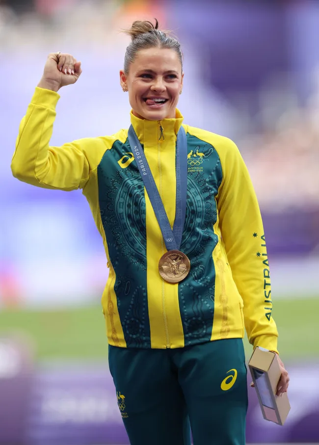 Australian athlete celebrates with a bronze medal, wearing a green and yellow jacket, fist raised in triumph.
