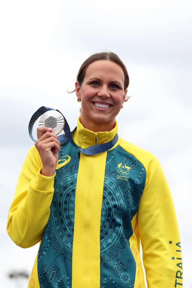 Australian athlete in yellow jacket proudly holds a silver medal, smiling at the camera.