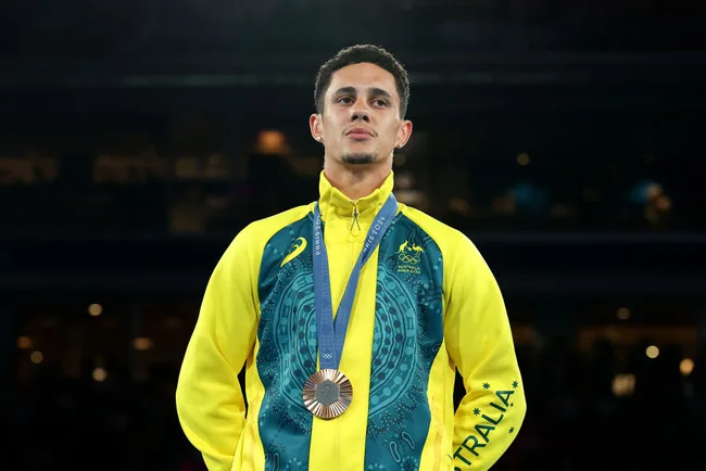 Athlete wearing a yellow Australian jacket stands with an Olympic medal around his neck.