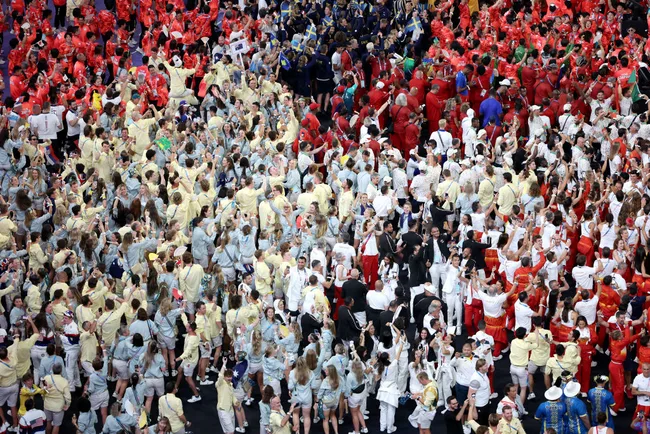 A crowd of athletes in colorful uniforms at the Tokyo 2020 Olympic Games opening ceremony, celebrating together.