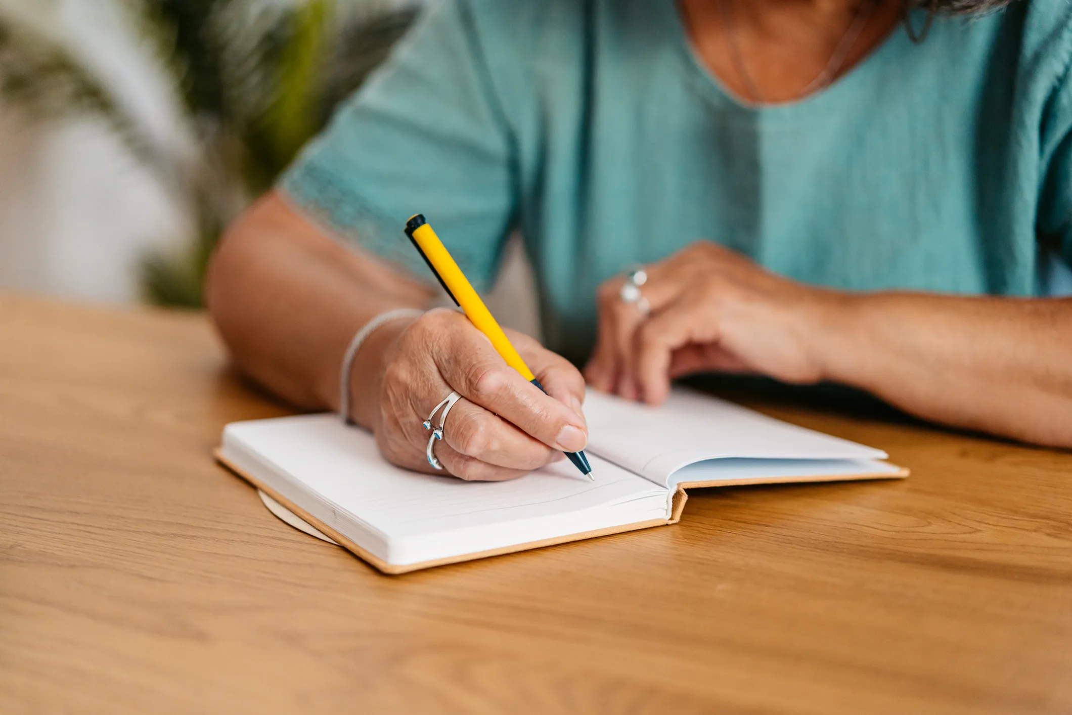 Mature woman writing in a notebook at the kitchen table at home. 