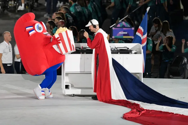 A person in a red costume with popcorn meets DJ in long red, white, and blue cape at the European Games ceremony.