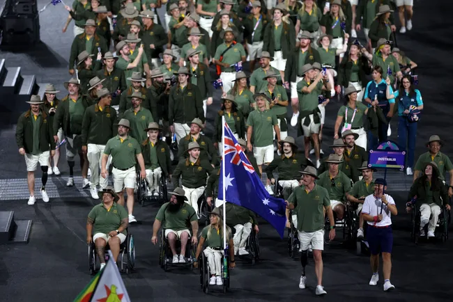 Australian team marching with their flag at an international event, featuring team members in green uniforms and hats.